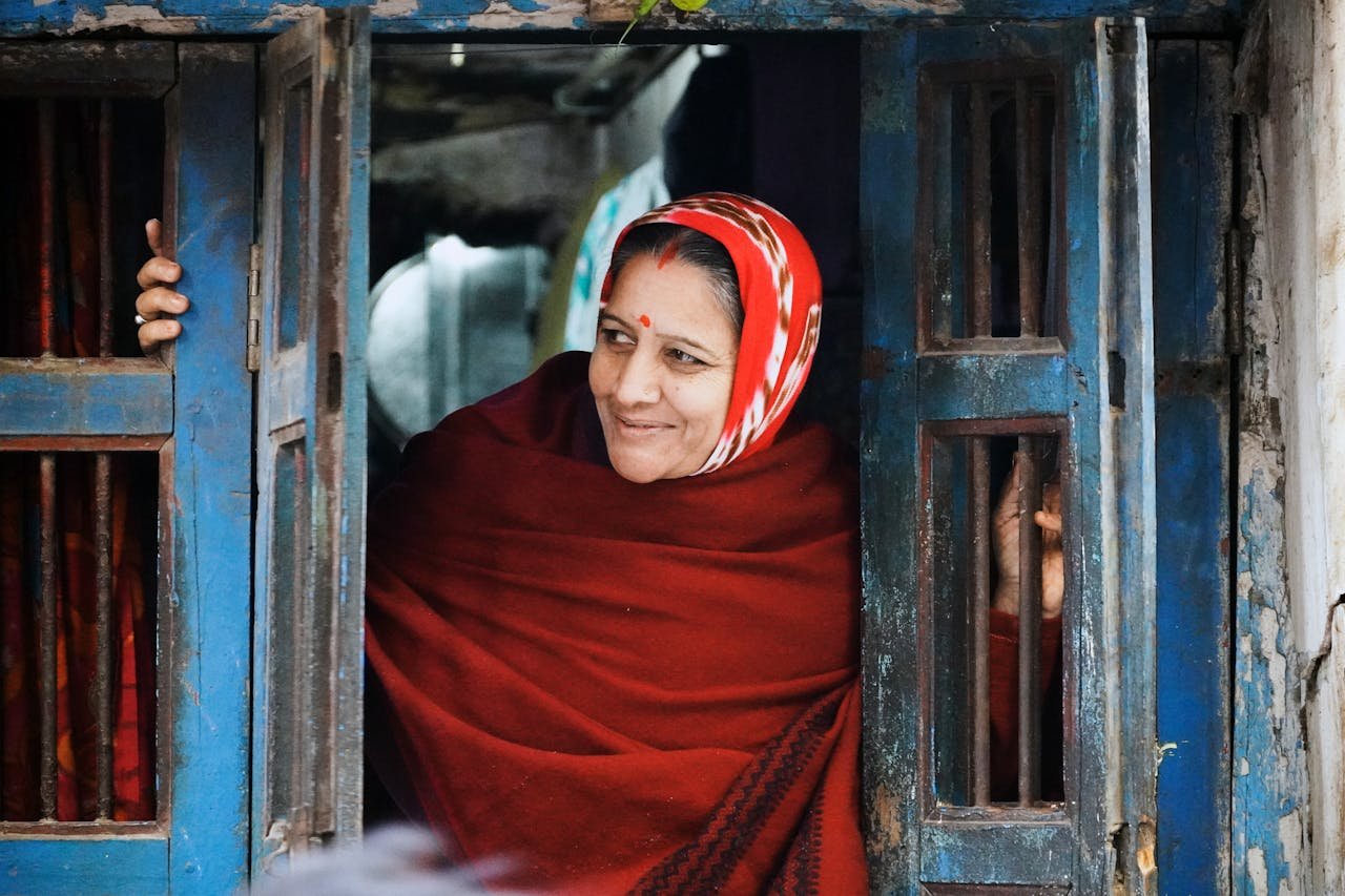 A Smiling Woman in a Headscarf Looking Out the Window